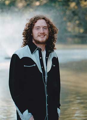 Danny Wayne Cotton in a dark western shirt, standing beside water